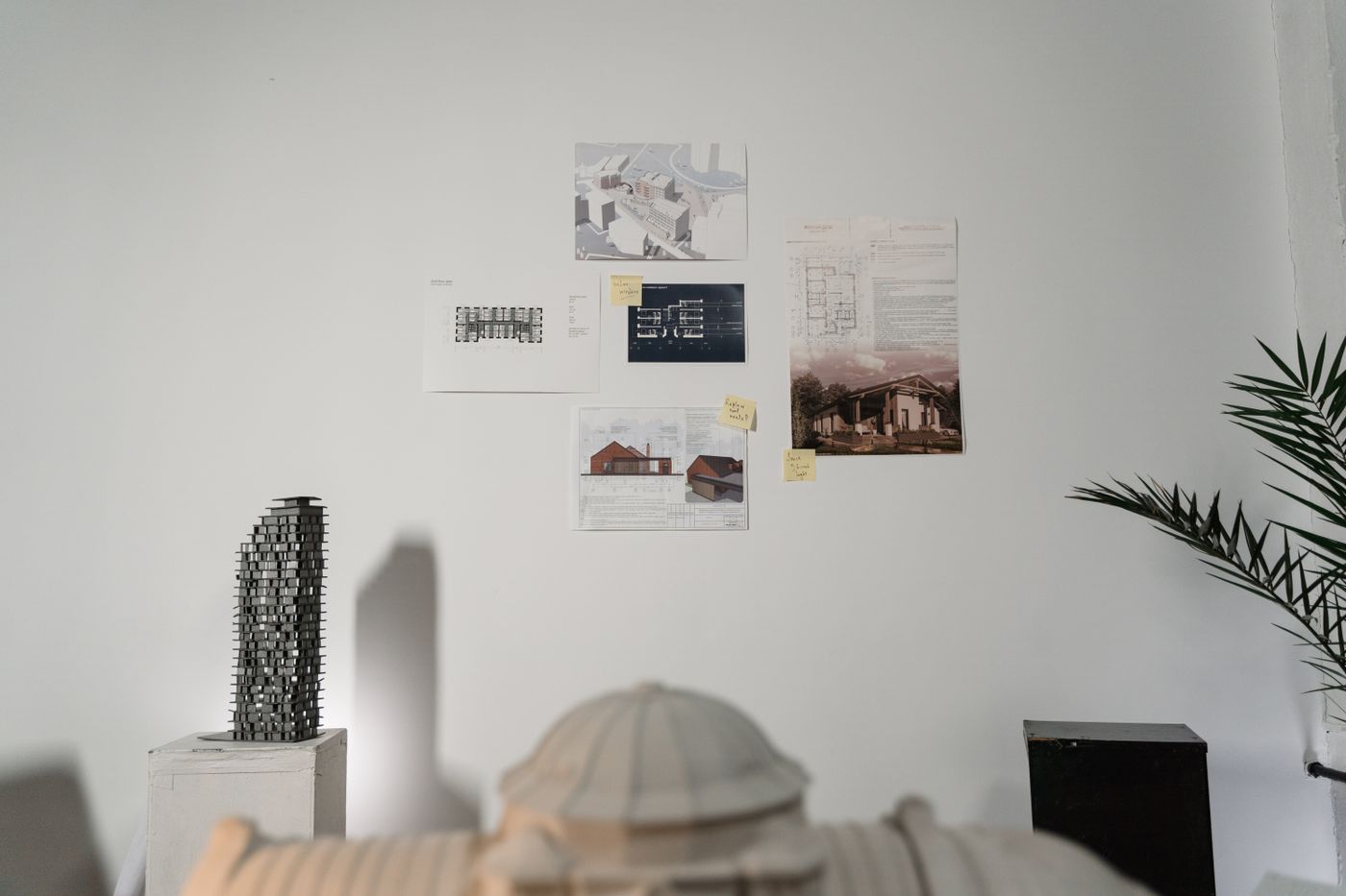 A studio wall of plans, elevations and models with handwritten notes pinned beside them.