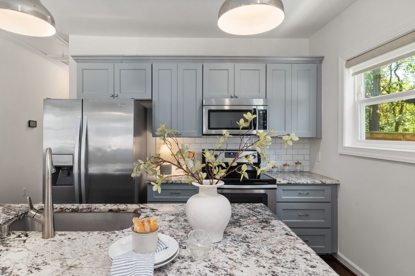 A staged kitchen with a granite island, styled counters and grey cabinetry.