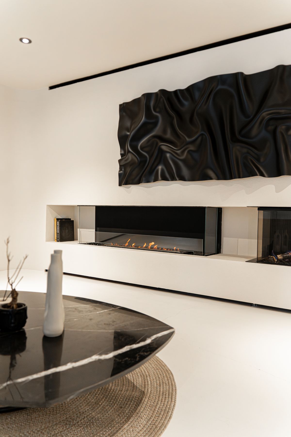 A sculptural fireplace wall in a minimal room with a black marble table.