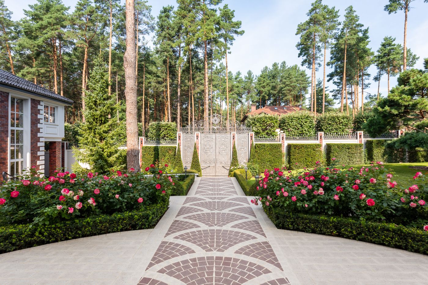 A formal garden with rose beds, clipped hedging and a patterned stone path to a gate.