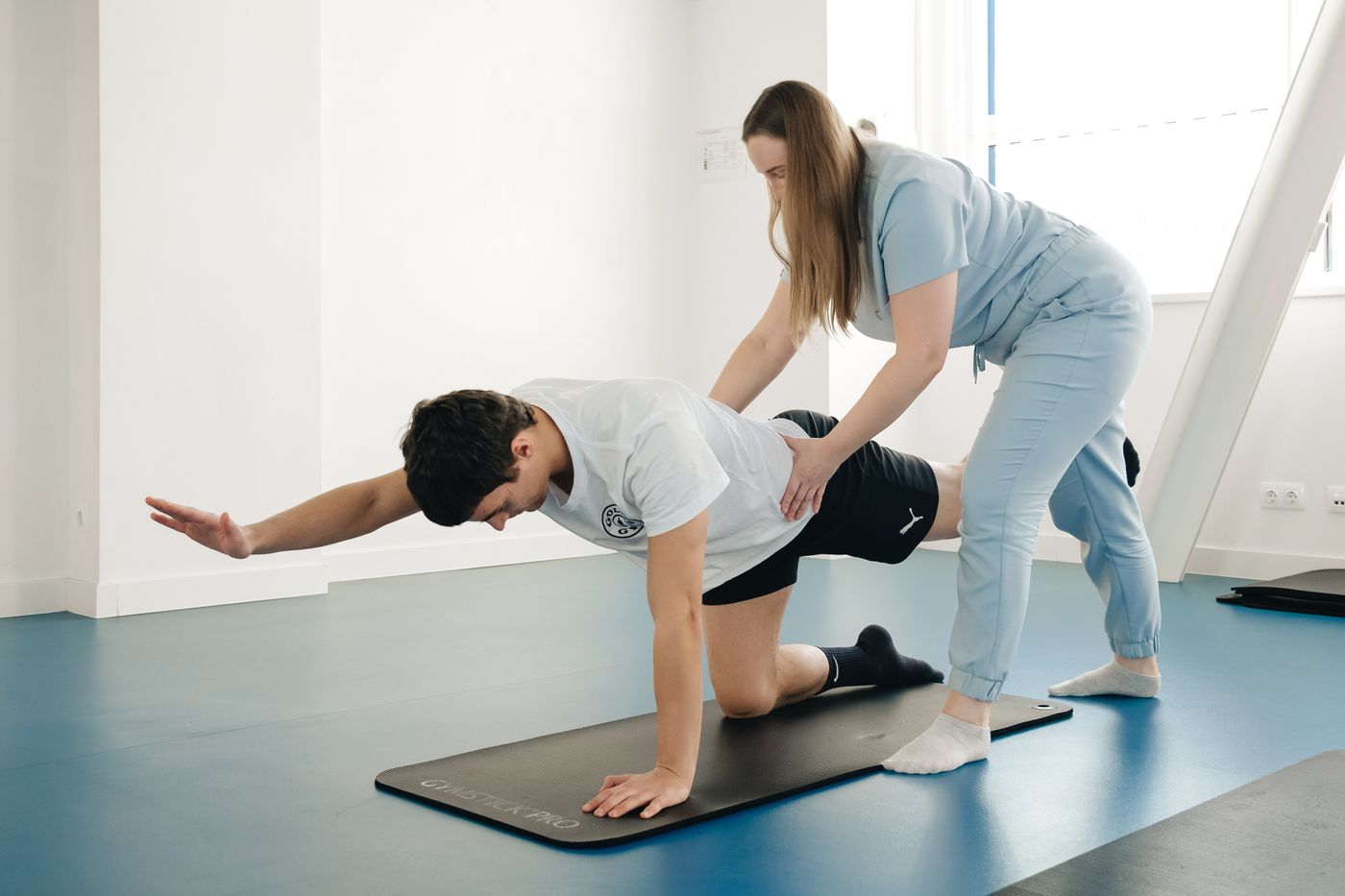 A physiotherapist correcting a patient's position during a floor exercise.
