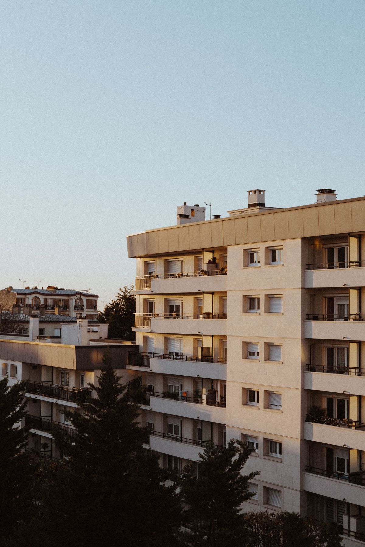 A pale apartment block with balconies at dusk.