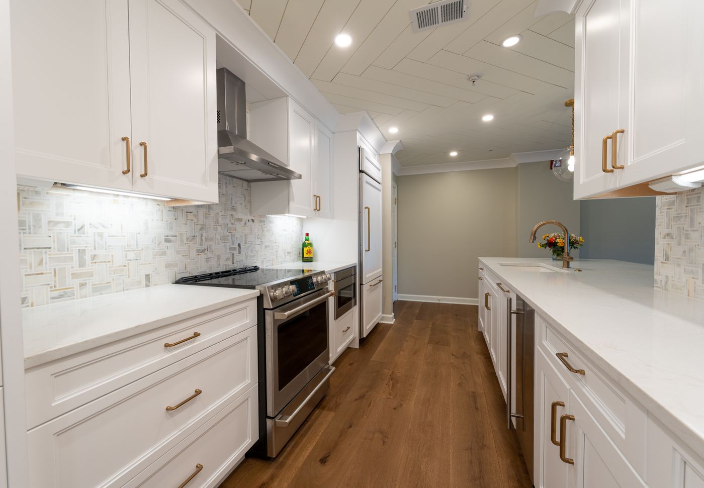 A finished galley kitchen with white shaker cabinets, brass hardware and a mosaic backsplash.