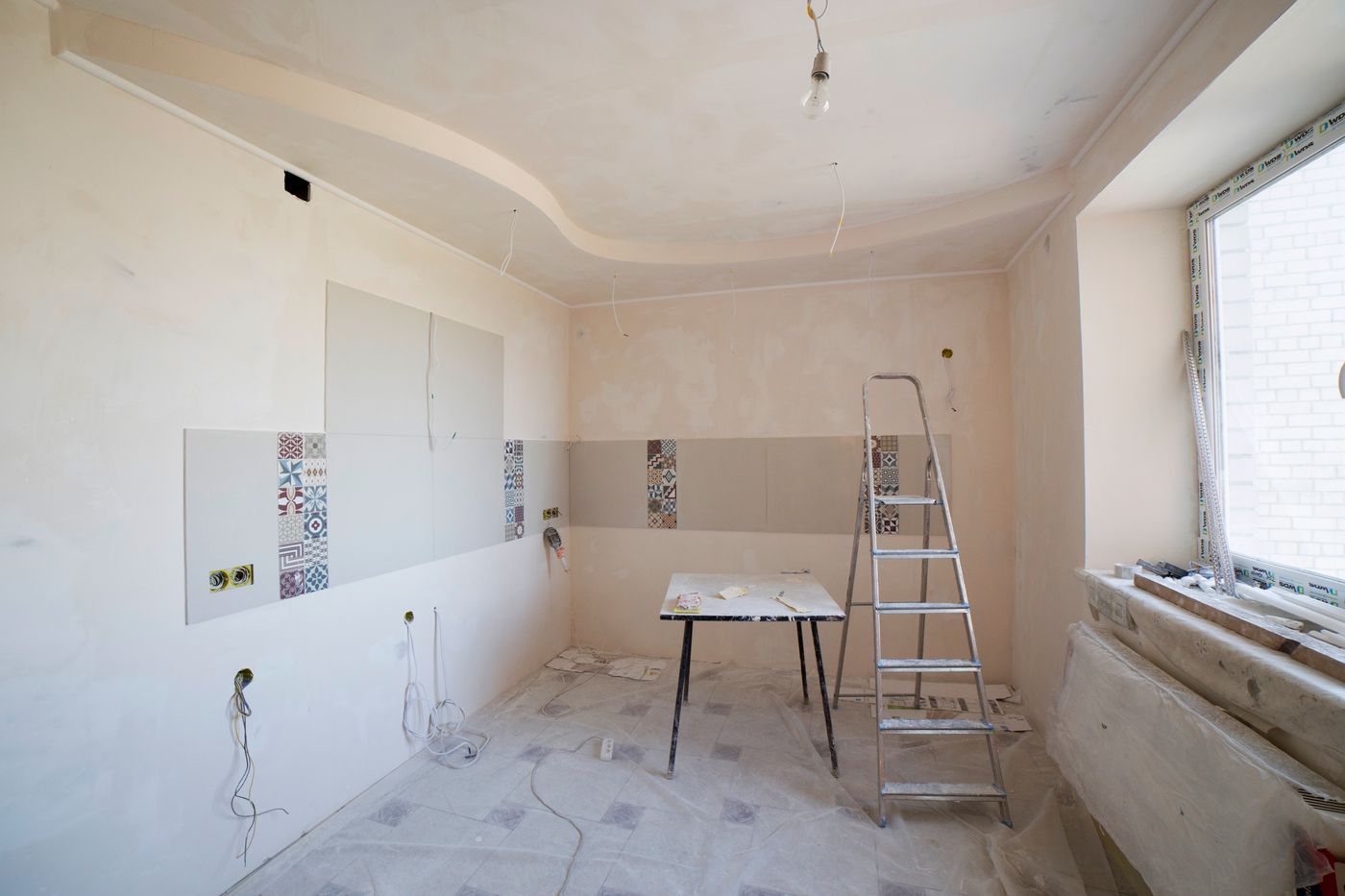A room mid-renovation with fresh plaster, tiling started and a stepladder in place.