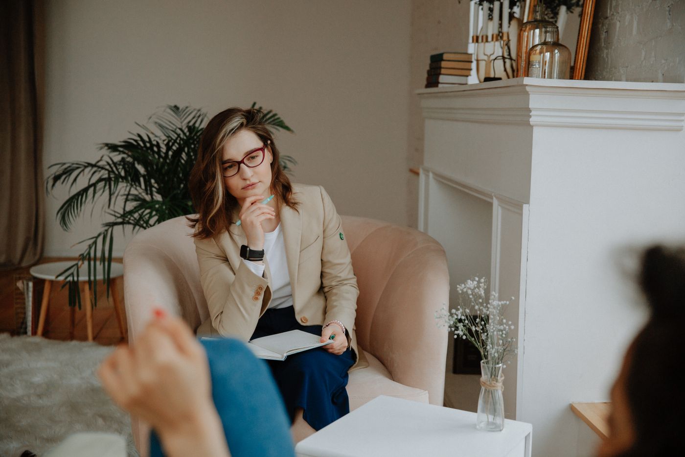 A therapist sitting with a notebook in an armchair in a calm room.