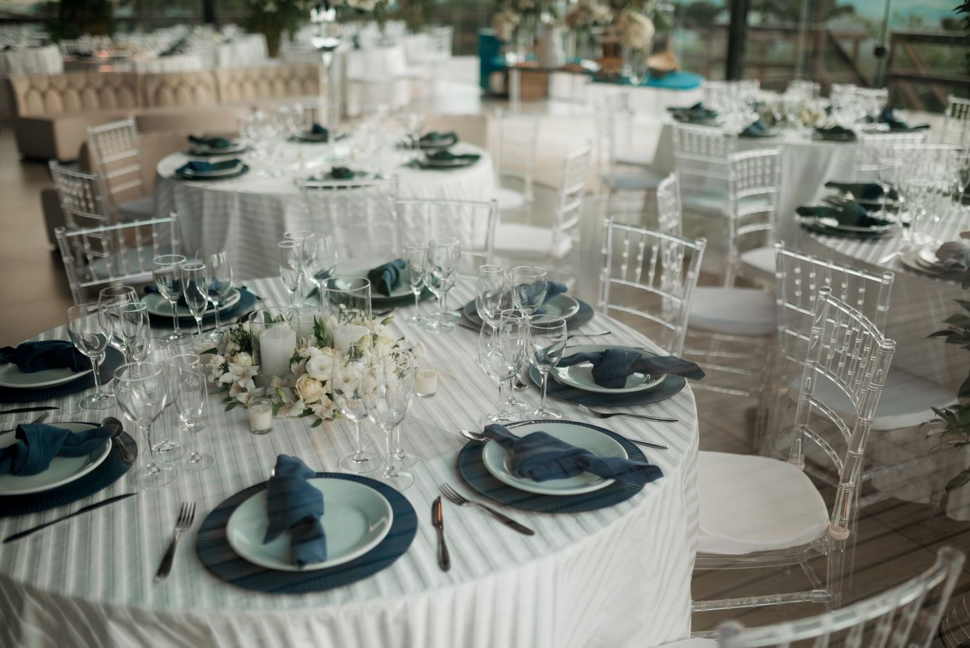Round tables laid with navy linen and white florals in a glazed reception room.